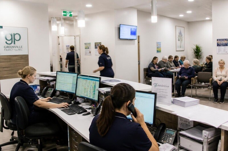 A practice manager at a clean desk in an Australian medical practice viewing a practice management software appointment book on screen