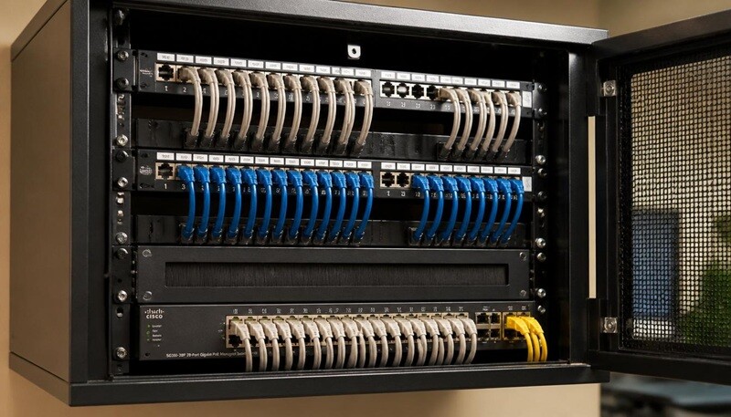 Wall-mounted comms cabinet with a labelled patch panel, Cisco managed switch and colour-coded structured cabling